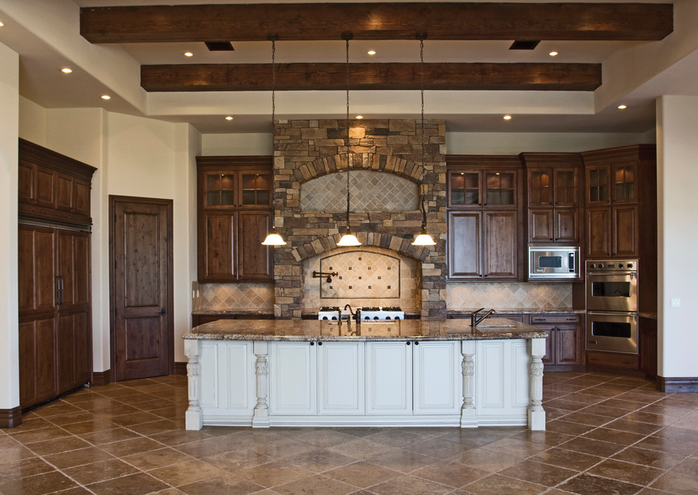 Inspiration for a mid-sized rustic single-wall travertine floor and brown floor eat-in kitchen remodel in Phoenix with an undermount sink, raised-panel cabinets, medium tone wood cabinets, granite countertops, beige backsplash, stone tile backsplash, stainless steel appliances and an island