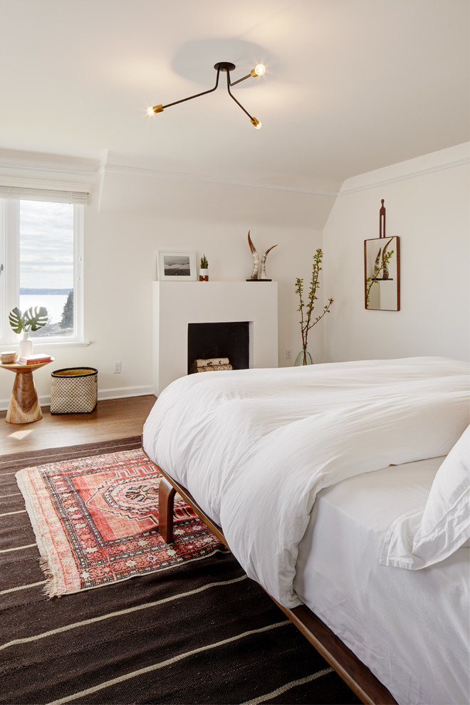 Photo of a midcentury bedroom in Seattle with white walls, dark hardwood floors, a plaster fireplace surround and brown floor.