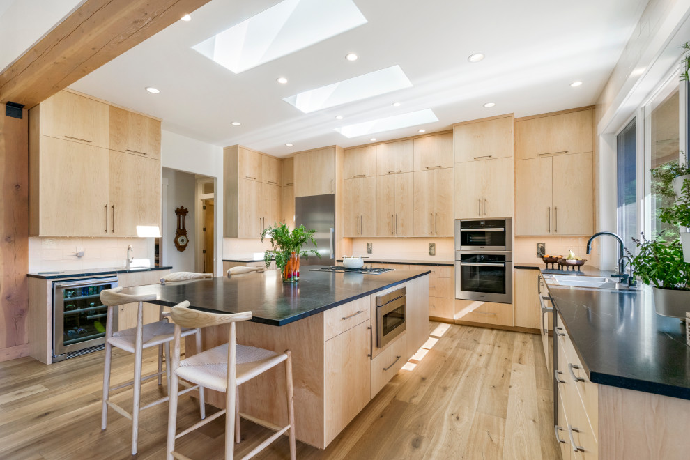 Design ideas for a contemporary u-shaped open plan kitchen in Seattle with a double-bowl sink, flat-panel cabinets, medium wood cabinets, stainless steel appliances, medium hardwood floors, with island, brown floor and black benchtop.