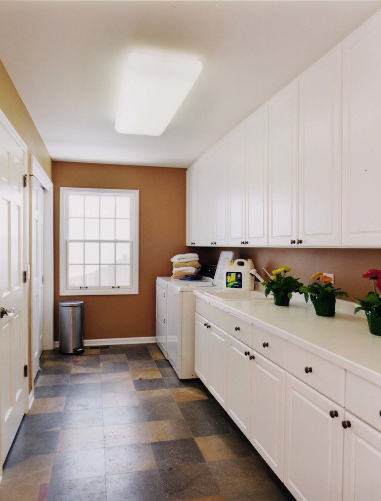 Design ideas for a mid-sized traditional single-wall utility room in Chicago with a drop-in sink, recessed-panel cabinets, white cabinets, solid surface benchtops, slate floors, a side-by-side washer and dryer and brown walls.