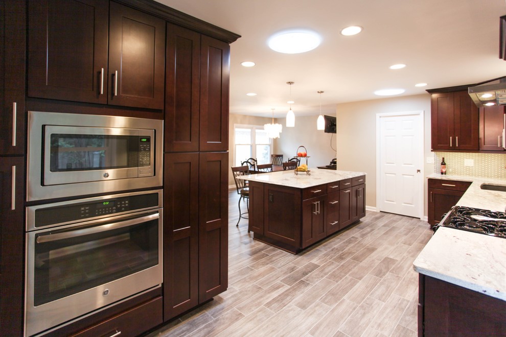 Eat-in kitchen - large transitional u-shaped porcelain tile eat-in kitchen idea in Chicago with an undermount sink, recessed-panel cabinets, dark wood cabinets, granite countertops, gray backsplash, glass tile backsplash, stainless steel appliances and an island
