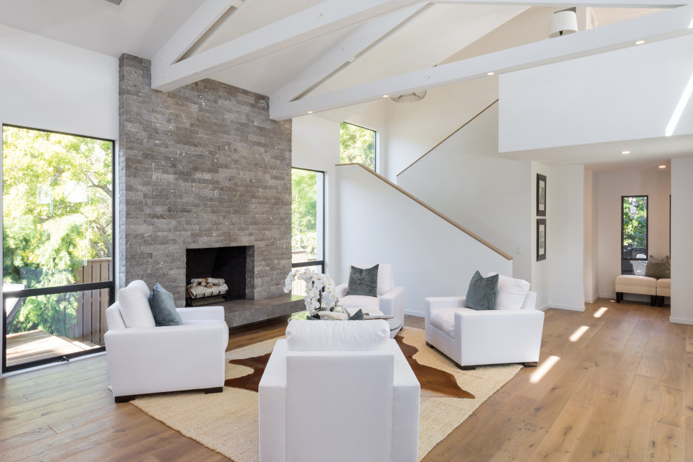 Design ideas for a midcentury formal open concept living room in Los Angeles with white walls, light hardwood floors, a standard fireplace, a stone fireplace surround, no tv and vaulted.