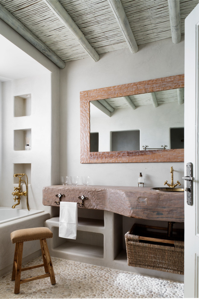 Inspiration for a coastal bathroom in Madrid with open cabinets, grey cabinets, an alcove bath, white walls, pebble tile flooring, a built-in sink, wooden worktops, beige floors, brown worktops, a wall niche, a single sink, a built in vanity unit, exposed beams and a wood ceiling.