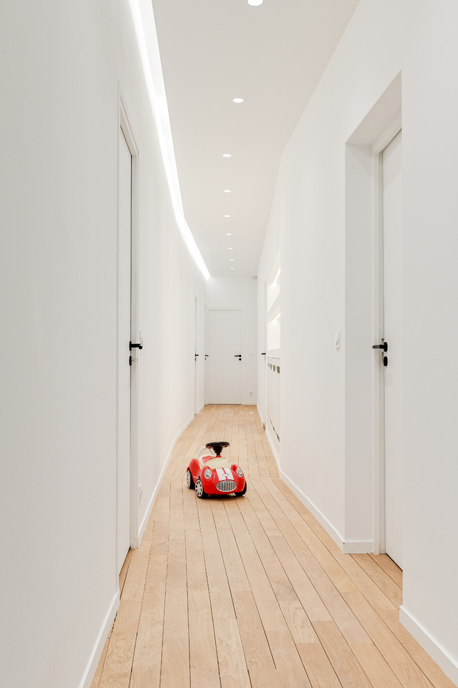 Expansive scandinavian hallway in Paris with white walls and light hardwood floors.