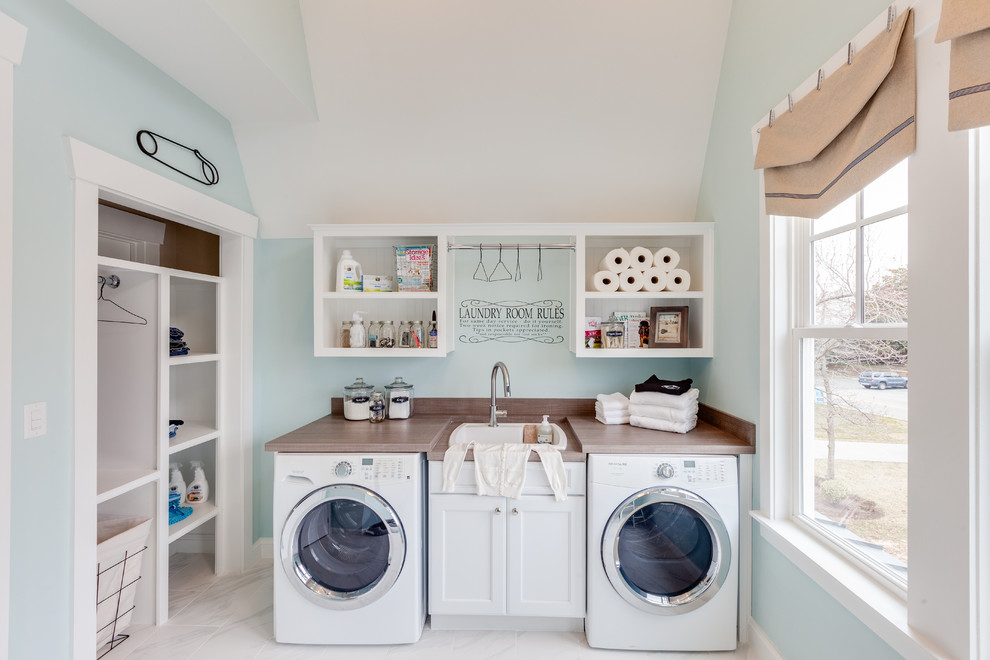 This is an example of a large beach style utility room in Other with a drop-in sink, recessed-panel cabinets, white cabinets, laminate benchtops, blue walls, marble floors and a side-by-side washer and dryer.