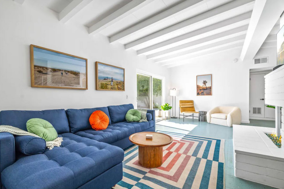 На фото: гостиная комната в стиле ретро с белыми стенами, полом из ламината, стандартным камином, фасадом камина из кирпича, телевизором на стене, синим полом и балками на потолке