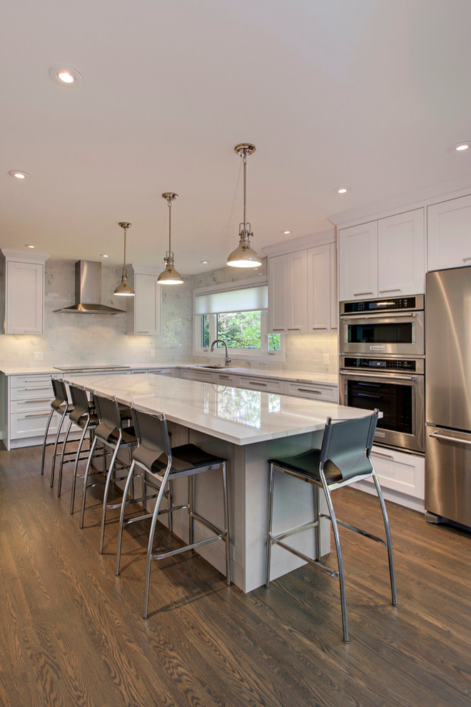 Example of a transitional l-shaped medium tone wood floor eat-in kitchen design in Calgary with an undermount sink, shaker cabinets, white cabinets, quartz countertops, white backsplash, porcelain backsplash, stainless steel appliances and an island