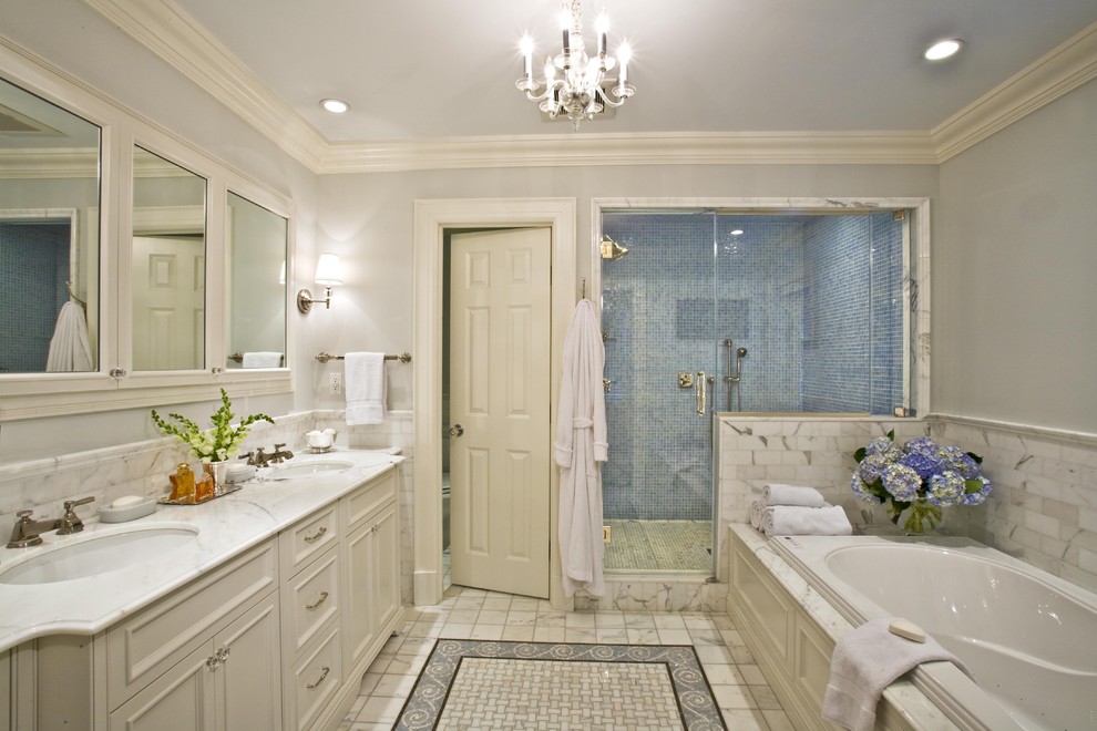 This is an example of a large traditional master bathroom in New York with an undermount sink, recessed-panel cabinets, white cabinets, an alcove tub, an alcove shower, gray tile, stone tile, grey walls and marble benchtops.