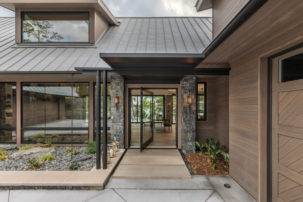 Inspiration pour une façade de maison marron design en bois et bardage à clin de taille moyenne et à deux étages et plus avec un toit à deux pans, un toit en métal et un toit marron.