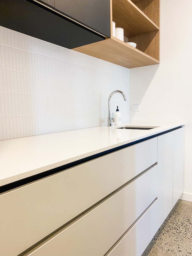 Inredning av ett modernt stort vit vitt kök, med en dubbel diskho, luckor med profilerade fronter, grå skåp, bänkskiva i kvarts, vitt stänkskydd, stänkskydd i keramik, svarta vitvaror, betonggolv, en köksö och grått golv