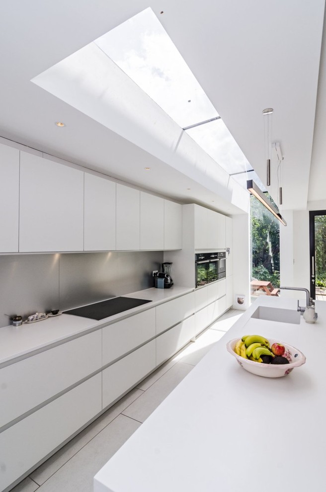 Photo of a large modern single-wall eat-in kitchen in London with an integrated sink, flat-panel cabinets, white cabinets, solid surface benchtops, white splashback, stainless steel appliances, porcelain floors and a peninsula.