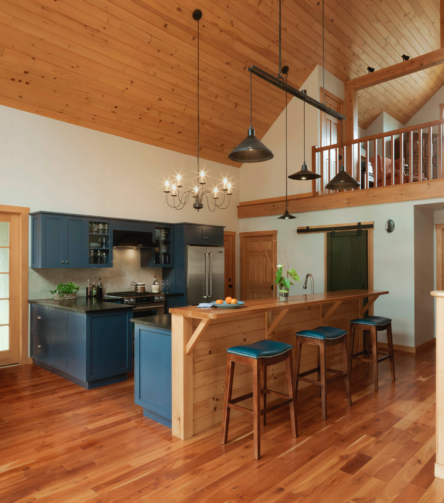 Inspiration for a mid-sized country l-shaped eat-in kitchen in Burlington with shaker cabinets, blue cabinets, stainless steel appliances, medium hardwood floors, with island, brown floor, solid surface benchtops, black benchtop and beige splashback.