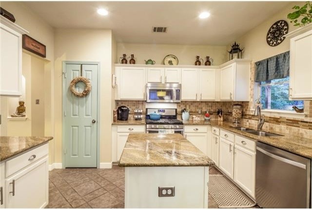 Small eclectic open plan kitchen in Austin with an undermount sink, shaker cabinets, yellow cabinets, granite benchtops, brown splashback, glass tile splashback, stainless steel appliances, porcelain floors and with island.