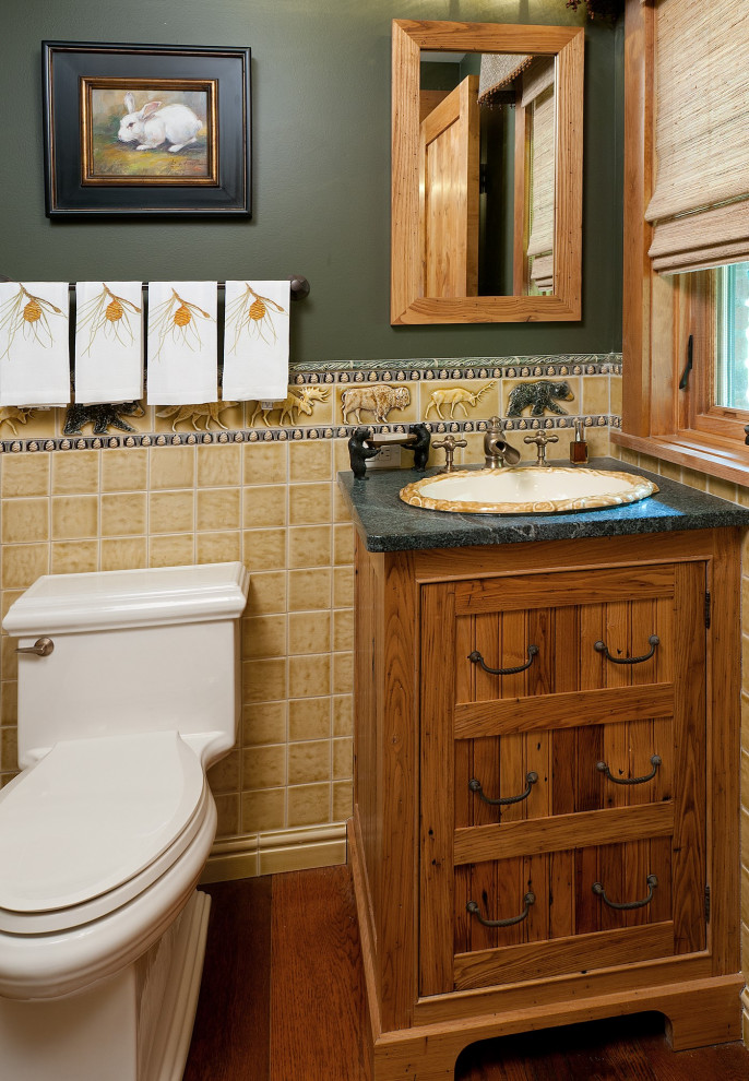Small traditional powder room with furniture-like cabinets, medium wood cabinets, a one-piece toilet, yellow tile, porcelain tile, green walls, medium hardwood floors, a drop-in sink, soapstone benchtops and green benchtops.