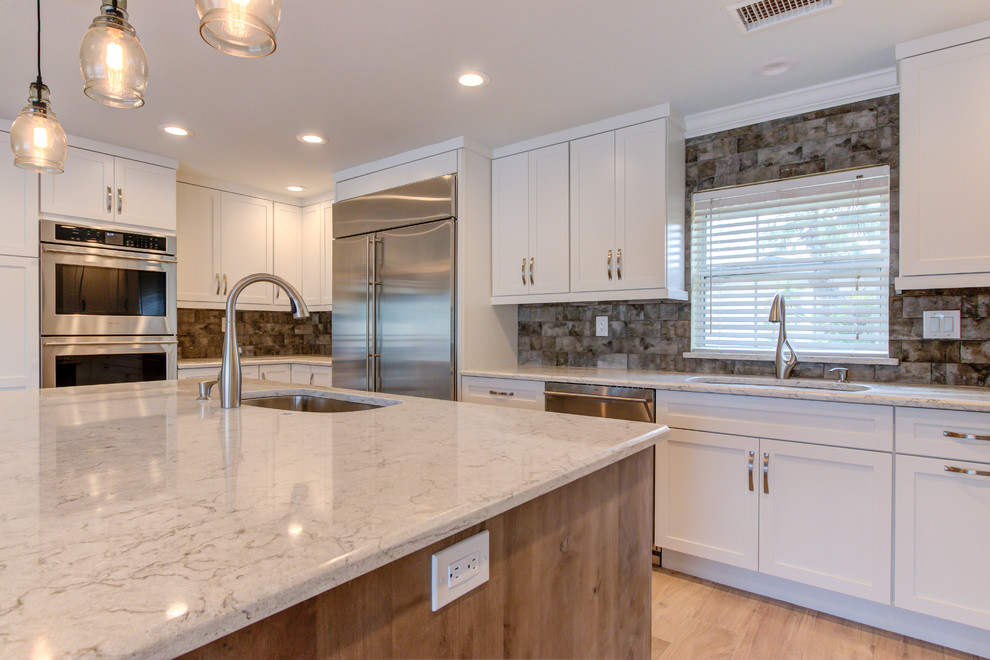 Large transitional u-shaped porcelain tile and brown floor enclosed kitchen photo with an undermount sink, shaker cabinets, white cabinets, quartz countertops, brown backsplash, stainless steel appliances, an island and beige countertops