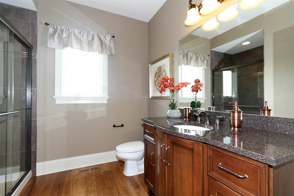 Inspiration for a large transitional bathroom in Chicago with an undermount sink, recessed-panel cabinets, medium wood cabinets, granite benchtops, an alcove shower, a one-piece toilet, beige walls and medium hardwood floors.