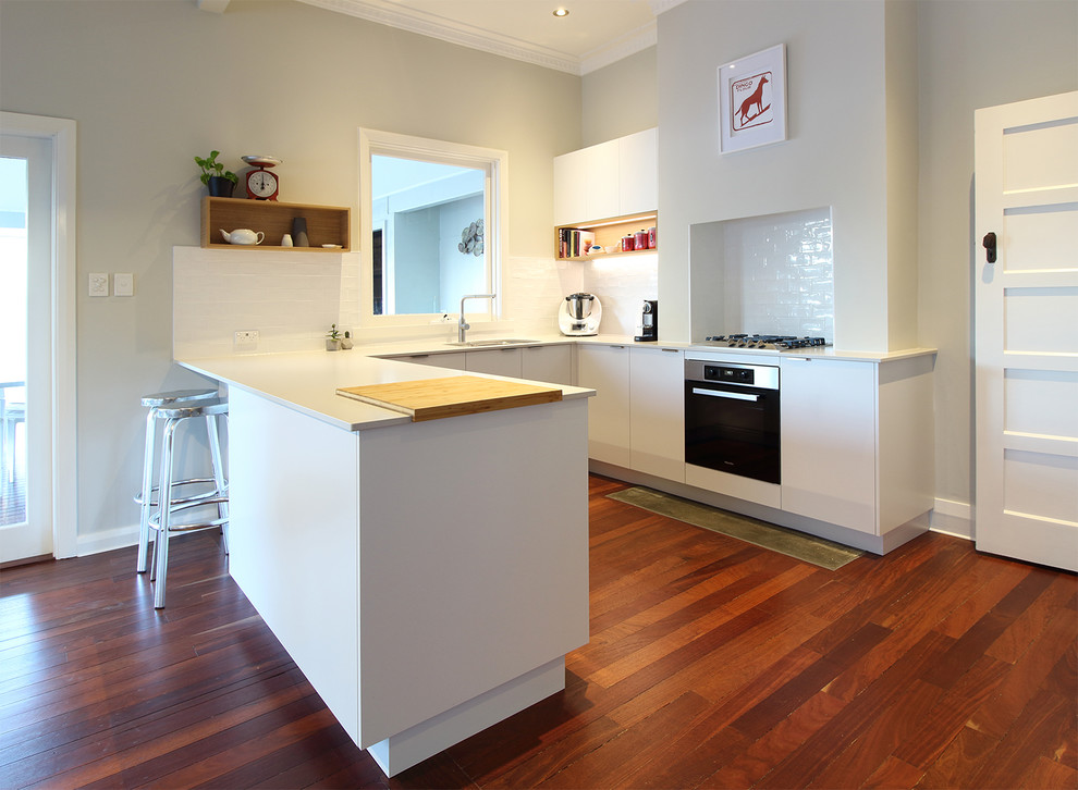 This is an example of a traditional u-shaped kitchen in Perth with white cabinets, white splashback, a peninsula, brown floor and white benchtop.