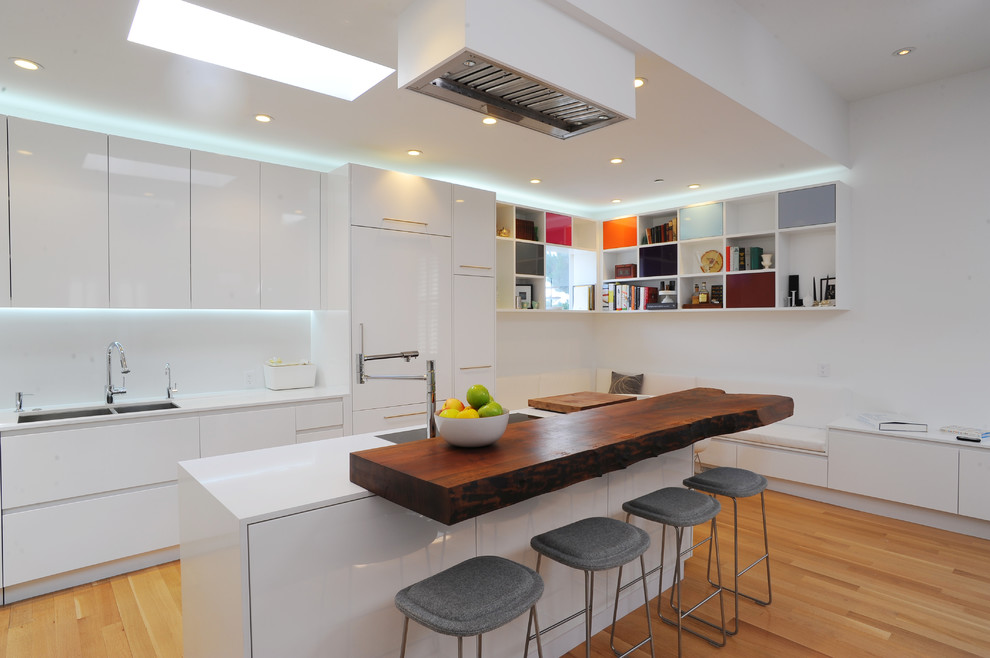 Design ideas for a contemporary galley kitchen in San Francisco with a double-bowl sink, flat-panel cabinets, white cabinets, wood benchtops, white splashback, panelled appliances, light hardwood floors, with island and white benchtop.