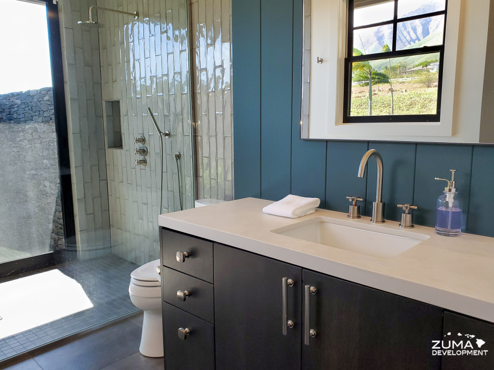 Inspiration for a mid-sized country 3/4 bathroom in Hawaii with flat-panel cabinets, black cabinets, a curbless shower, a two-piece toilet, white tile, porcelain tile, blue walls, ceramic floors, an undermount sink, engineered quartz benchtops, grey floor, an open shower and white benchtops.