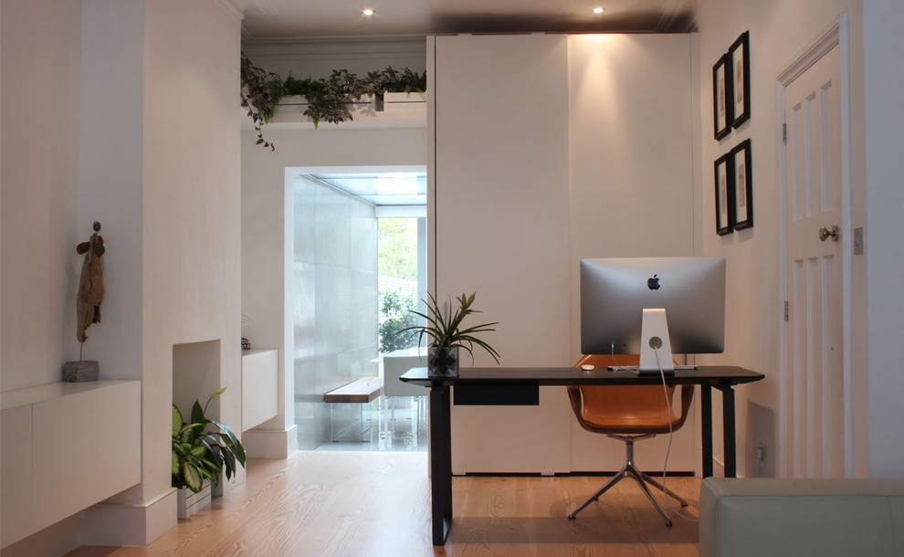 This is an example of a mid-sized modern home office in London with medium hardwood floors.