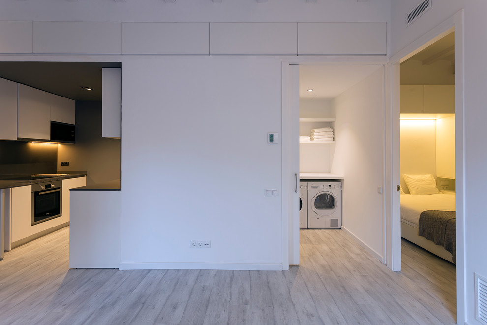 Photo of a mid-sized contemporary dedicated laundry room in Barcelona with open cabinets, white cabinets, white walls, light hardwood floors and a side-by-side washer and dryer.