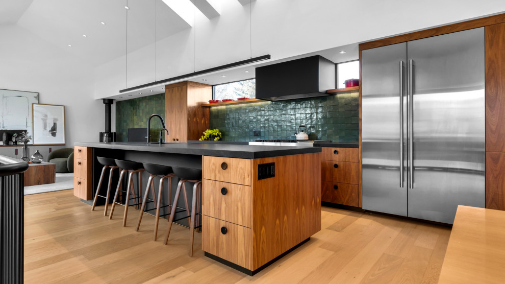 Bild på ett funkis svart svart kök, med en undermonterad diskho, släta luckor, skåp i mellenmörkt trä, bänkskiva i kvarts, grönt stänkskydd, stänkskydd i porslinskakel, rostfria vitvaror, ljust trägolv, en köksö och beiget golv