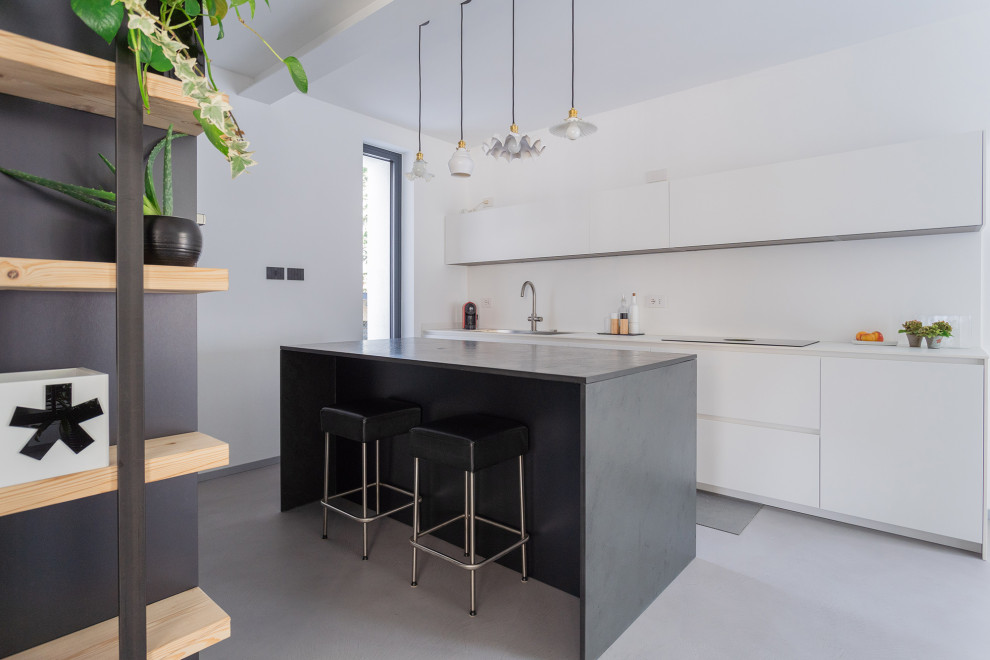 This is an example of a mid-sized contemporary galley open plan kitchen in Milan with a drop-in sink, flat-panel cabinets, white cabinets, solid surface benchtops, white splashback, stainless steel appliances, with island, grey floor and white benchtop.