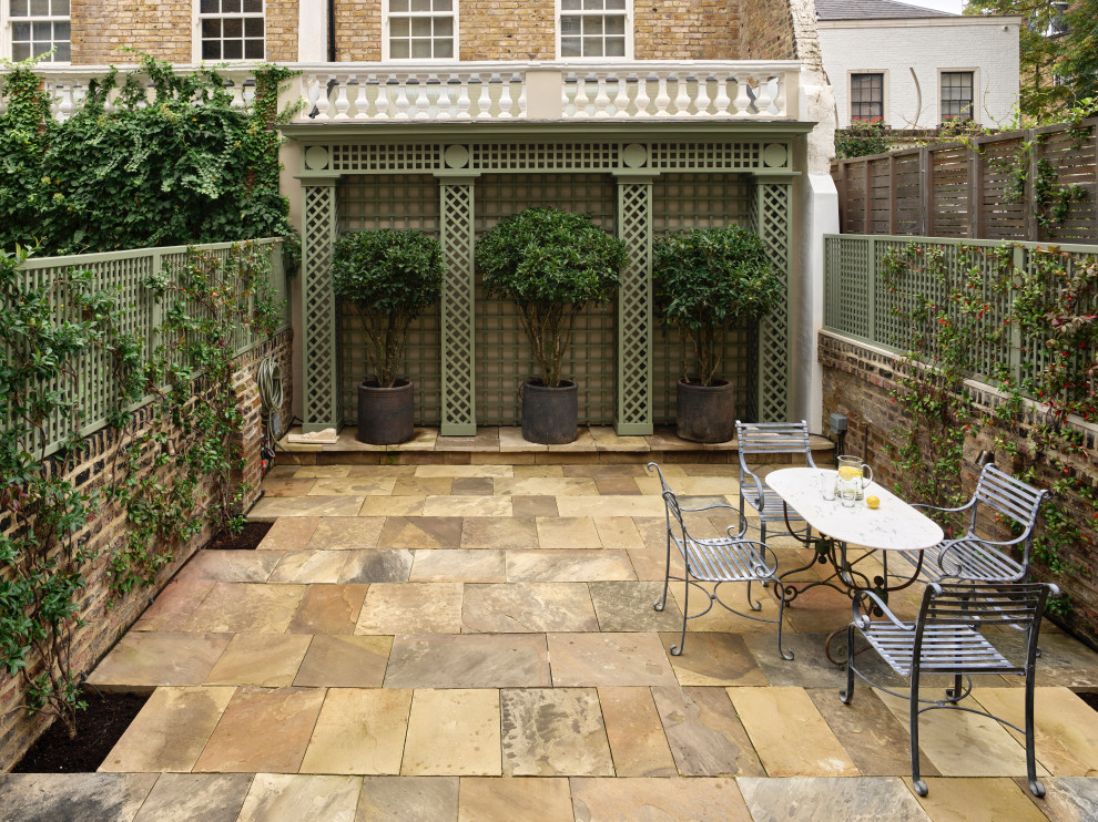 This is an example of a large victorian back patio in London with a potted garden, natural stone paving and no cover.