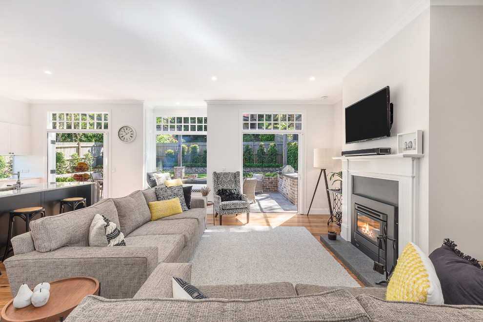 Mid-sized transitional formal open concept living room in Sydney with white walls, medium hardwood floors, a standard fireplace, a metal fireplace surround, a wall-mounted tv and brown floor.