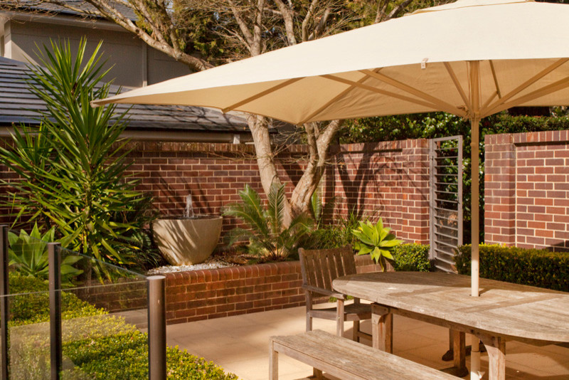 Mid-sized contemporary courtyard patio in Sydney with a water feature, natural stone pavers and an awning.