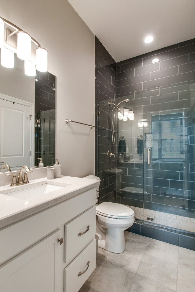 Photo of a mid-sized transitional 3/4 bathroom in Nashville with glass-front cabinets, white cabinets, gray tile, grey walls, ceramic floors, engineered quartz benchtops, multi-coloured floor, a hinged shower door, white benchtops, a single vanity, a built-in vanity, an alcove shower, a two-piece toilet, an undermount sink and vaulted.
