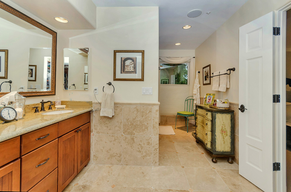 Photo of a mid-sized transitional master bathroom in Phoenix with an undermount sink, shaker cabinets, brown cabinets, granite benchtops, an alcove shower, a one-piece toilet, beige tile, stone tile, beige walls and travertine floors.
