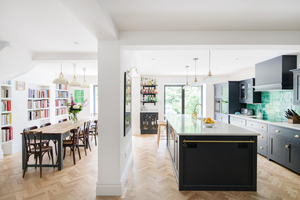 This is an example of a contemporary eat-in kitchen in London with a double-bowl sink, black cabinets, tile benchtops, green splashback, porcelain splashback, coloured appliances, light hardwood floors, with island, brown floor and white benchtop.