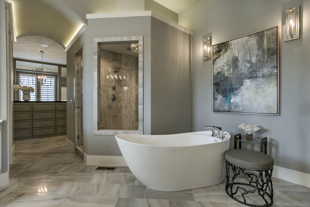 This is an example of a large contemporary master bathroom in Kansas City with shaker cabinets, white cabinets, a freestanding tub, an alcove shower, gray tile, porcelain tile, grey walls, marble floors, an undermount sink, marble benchtops, grey floor, a hinged shower door, white benchtops, an enclosed toilet, a double vanity and a built-in vanity.