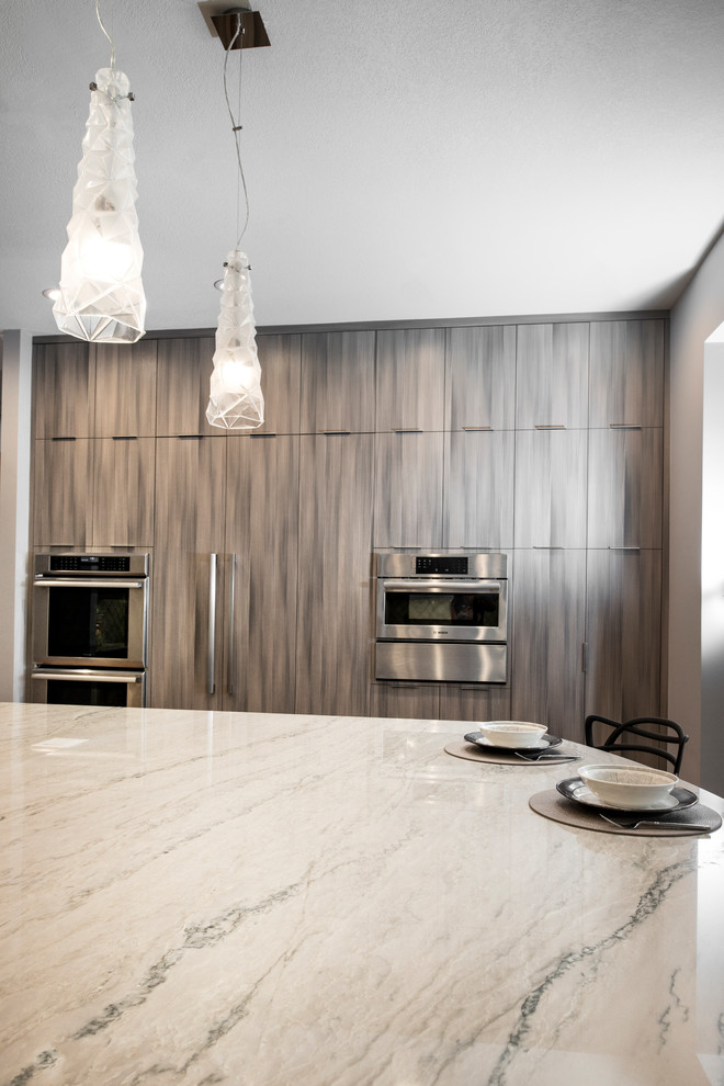 Example of a large transitional medium tone wood floor and brown floor open concept kitchen design with an undermount sink, flat-panel cabinets, brown cabinets, quartzite countertops, white backsplash, ceramic backsplash, stainless steel appliances, an island and beige countertops