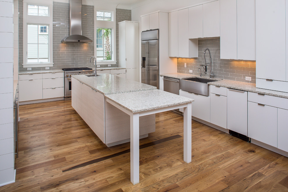 Photo of a mid-sized modern u-shaped eat-in kitchen in Charleston with a farmhouse sink, flat-panel cabinets, white cabinets, recycled glass benchtops, brown splashback, subway tile splashback, stainless steel appliances, medium hardwood floors and with island.