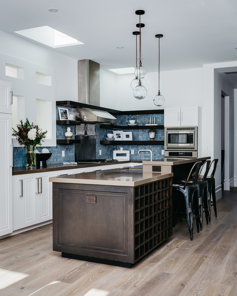 Inspiration for a mid-sized transitional l-shaped eat-in kitchen in San Francisco with granite benchtops, blue splashback, glass tile splashback, stainless steel appliances, light hardwood floors, with island, beige floor, an undermount sink, open cabinets, dark wood cabinets and brown benchtop.