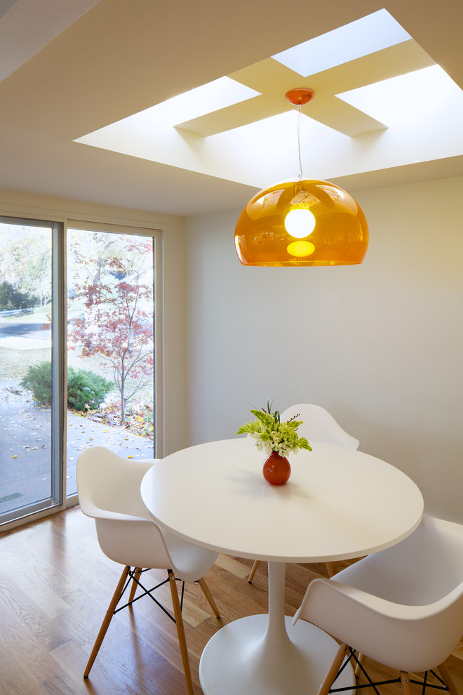 This is an example of a midcentury dining room in Denver with white walls and medium hardwood floors.