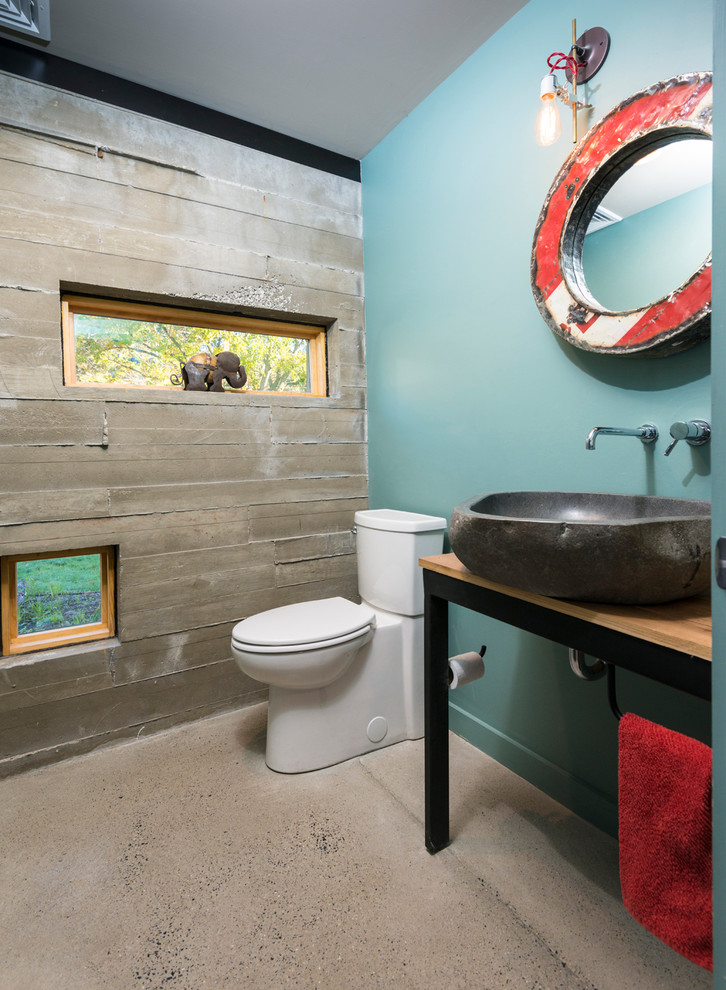 Photo of a small industrial powder room in Philadelphia with a two-piece toilet, blue walls, concrete floors, a vessel sink, black cabinets, wood benchtops, beige floor and brown benchtops.