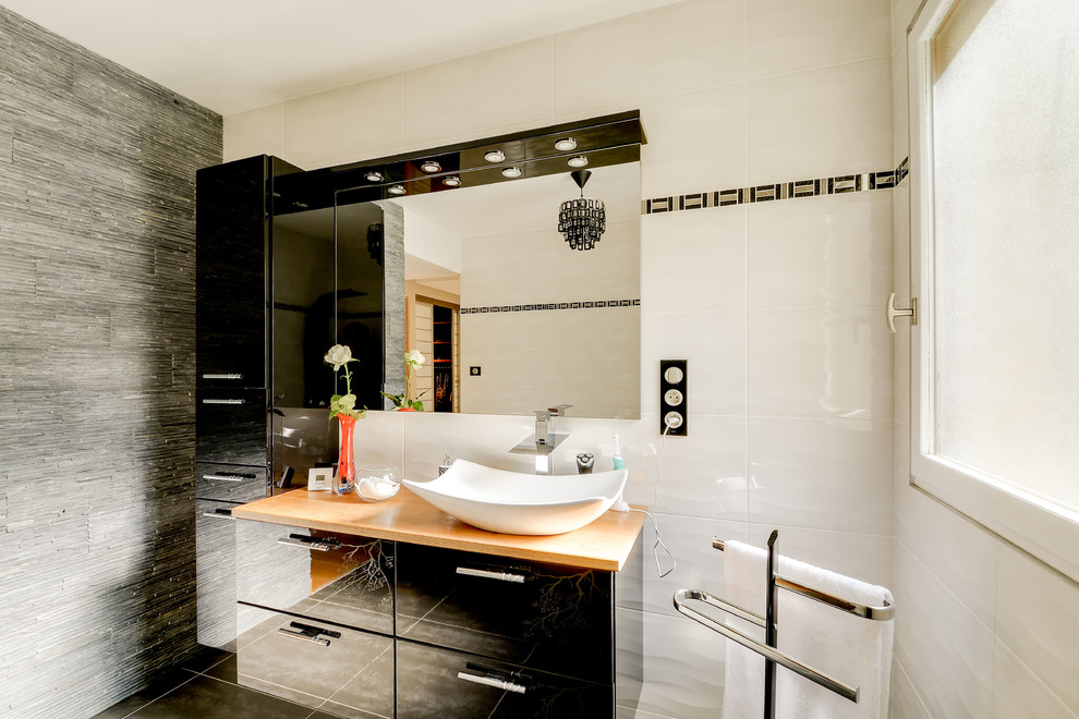 This is an example of a mid-sized contemporary master bathroom in Other with raised-panel cabinets, black cabinets, a curbless shower, white tile, ceramic tile, white walls, ceramic floors, a vessel sink, wood benchtops, grey floor and an open shower.