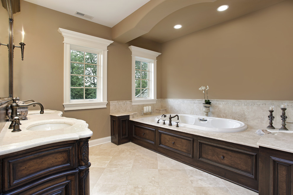 This is an example of a large traditional master bathroom in Atlanta with an undermount sink, furniture-like cabinets, dark wood cabinets, marble benchtops, a drop-in tub, a corner shower, a two-piece toilet, beige tile, stone tile, brown walls and travertine floors.