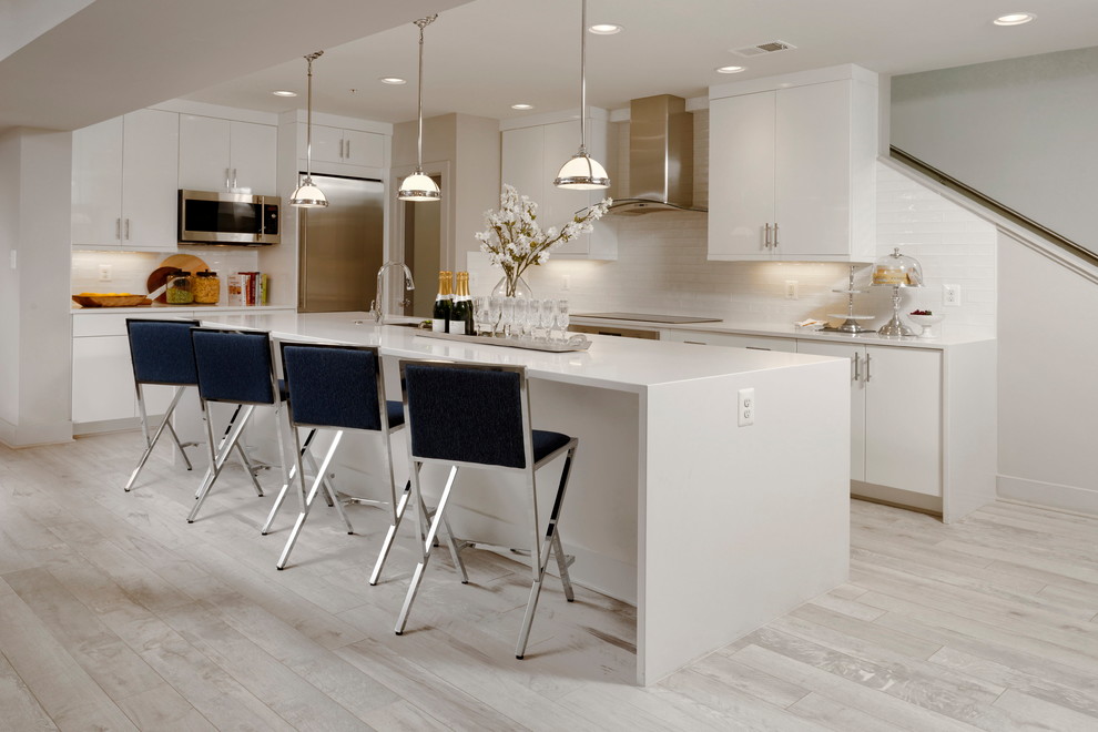 Design ideas for a contemporary kitchen in DC Metro with an undermount sink, flat-panel cabinets, white cabinets, white splashback, stainless steel appliances, light hardwood floors, with island and white benchtop.