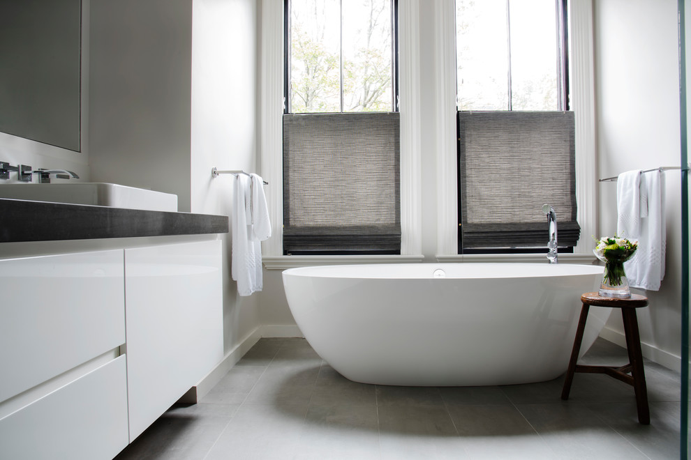 Mid-sized transitional master gray tile porcelain tile and gray floor freestanding bathtub photo in Boston with flat-panel cabinets, white cabinets, gray walls, a vessel sink and quartz countertops