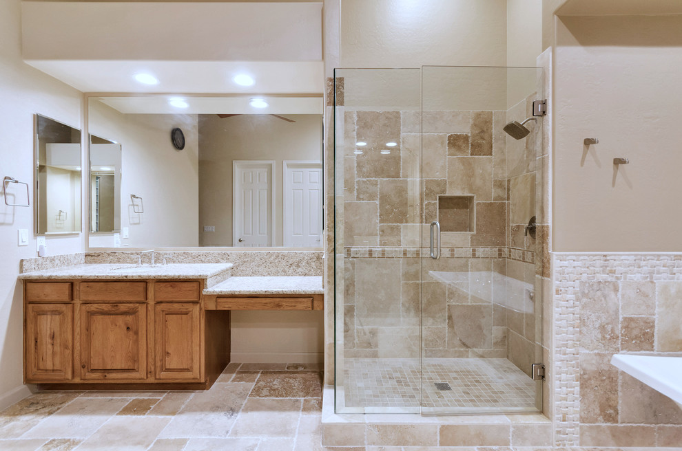Large traditional master bathroom in Phoenix with raised-panel cabinets, medium wood cabinets, a freestanding tub, a corner shower, brown tile, travertine, brown walls, travertine floors, granite benchtops, brown floor, a hinged shower door and an undermount sink.