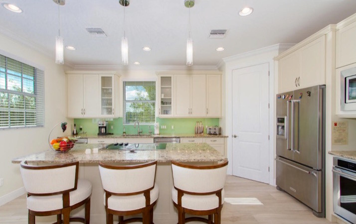 Inspiration for a mid-sized beach style u-shaped eat-in kitchen in Miami with a double-bowl sink, raised-panel cabinets, white cabinets, laminate benchtops, green splashback, stainless steel appliances, light hardwood floors, with island and beige floor.