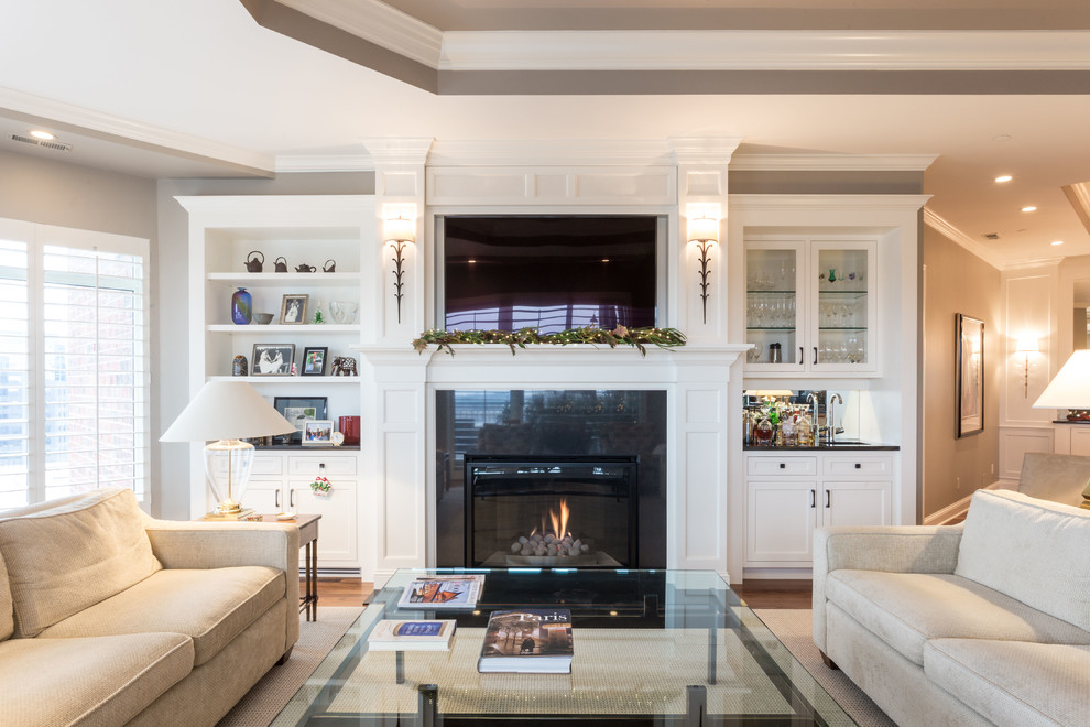 Photo of a mid-sized traditional formal open concept living room in Minneapolis with grey walls, medium hardwood floors, a standard fireplace, a wood fireplace surround and a wall-mounted tv.
