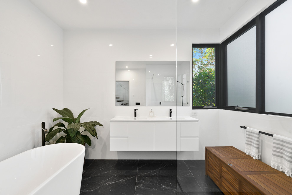 This is an example of a contemporary bathroom in Sunshine Coast with flat-panel cabinets, white cabinets, a freestanding tub, white walls, an integrated sink, grey floor and white benchtops.