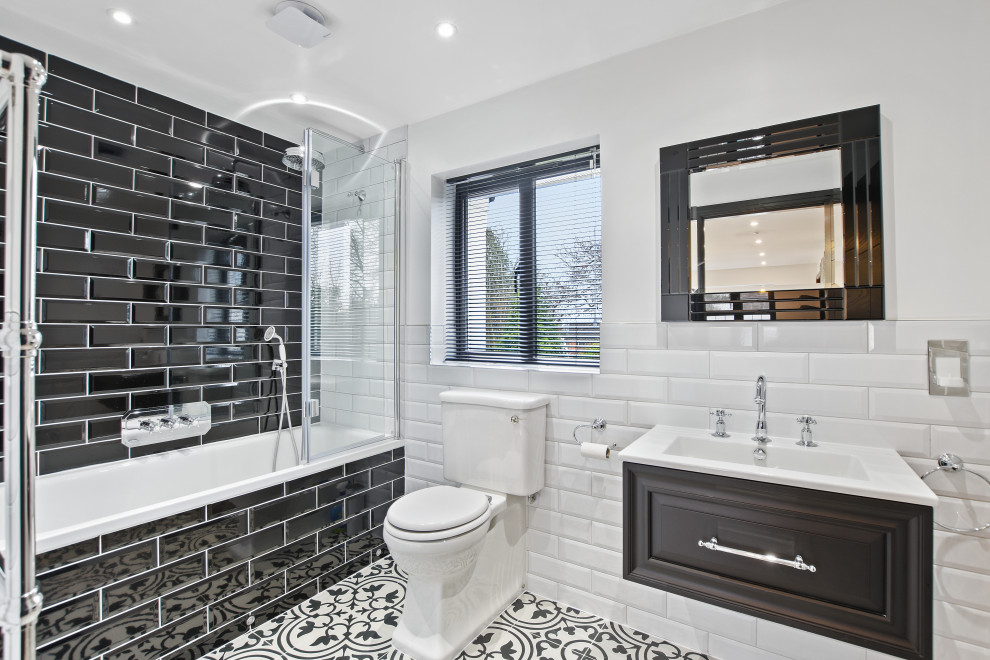 This is an example of a mid-sized contemporary 3/4 bathroom in London with raised-panel cabinets, black cabinets, a shower/bathtub combo, black tile, white walls, an integrated sink, multi-coloured floor, white benchtops, a single vanity and a floating vanity.