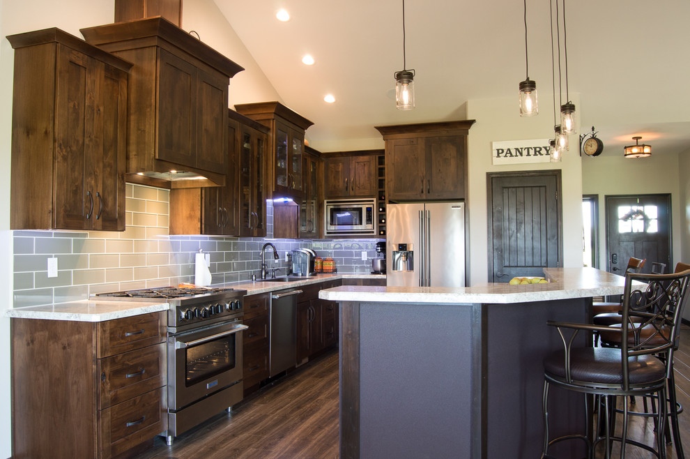 Example of a mountain style l-shaped brown floor eat-in kitchen design with shaker cabinets, brown cabinets, laminate countertops, gray backsplash, stainless steel appliances, an island and beige countertops