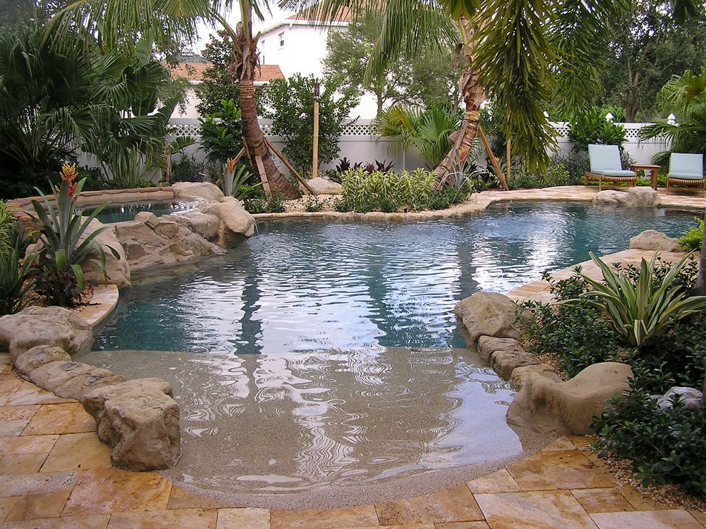 Design ideas for a tropical backyard custom-shaped natural pool in Miami with a hot tub and natural stone pavers.